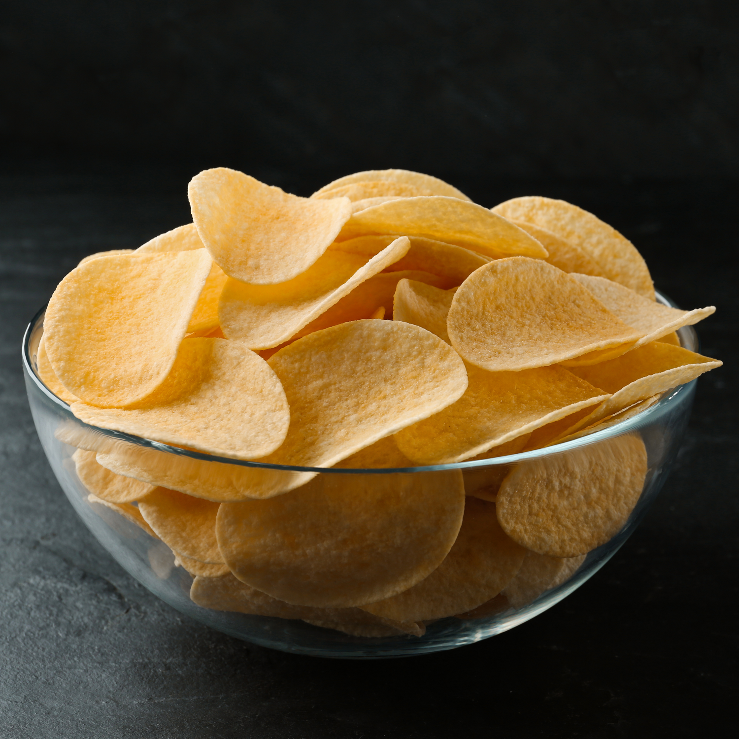 Bowl of stacked potato chips on a black background.