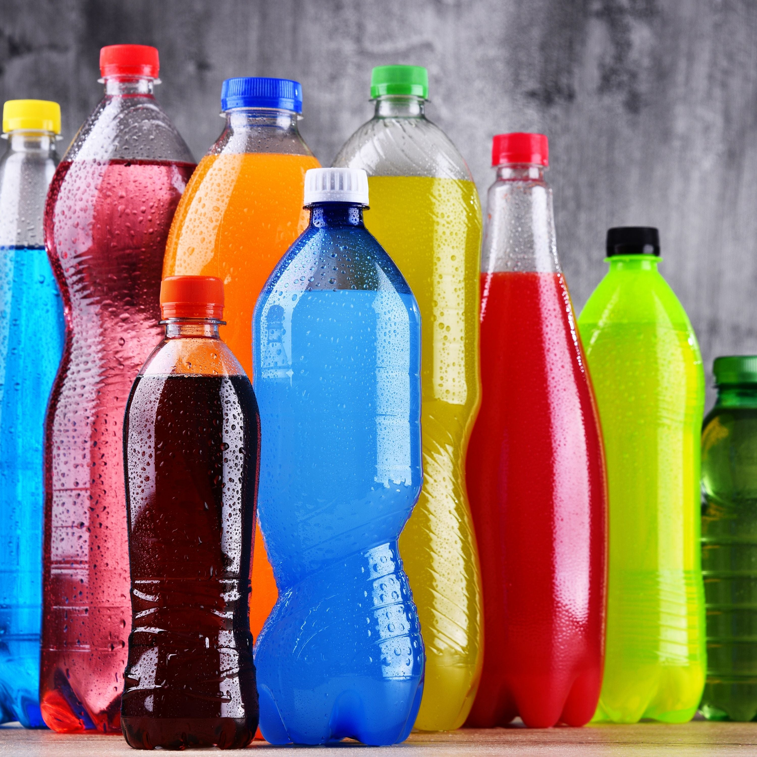 Assortment of colorful plastic bottles containing various drinks on a grey background.
